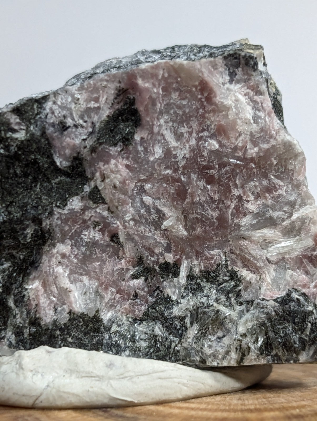 A rough, irregularly shaped piece of pinkish-purple rose quartz with translucent crystalline facets and dark gray matrix material.