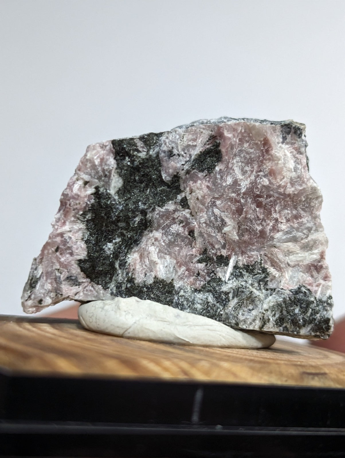 A rough, irregularly shaped piece of pink and black mineral rock with a crystalline texture.