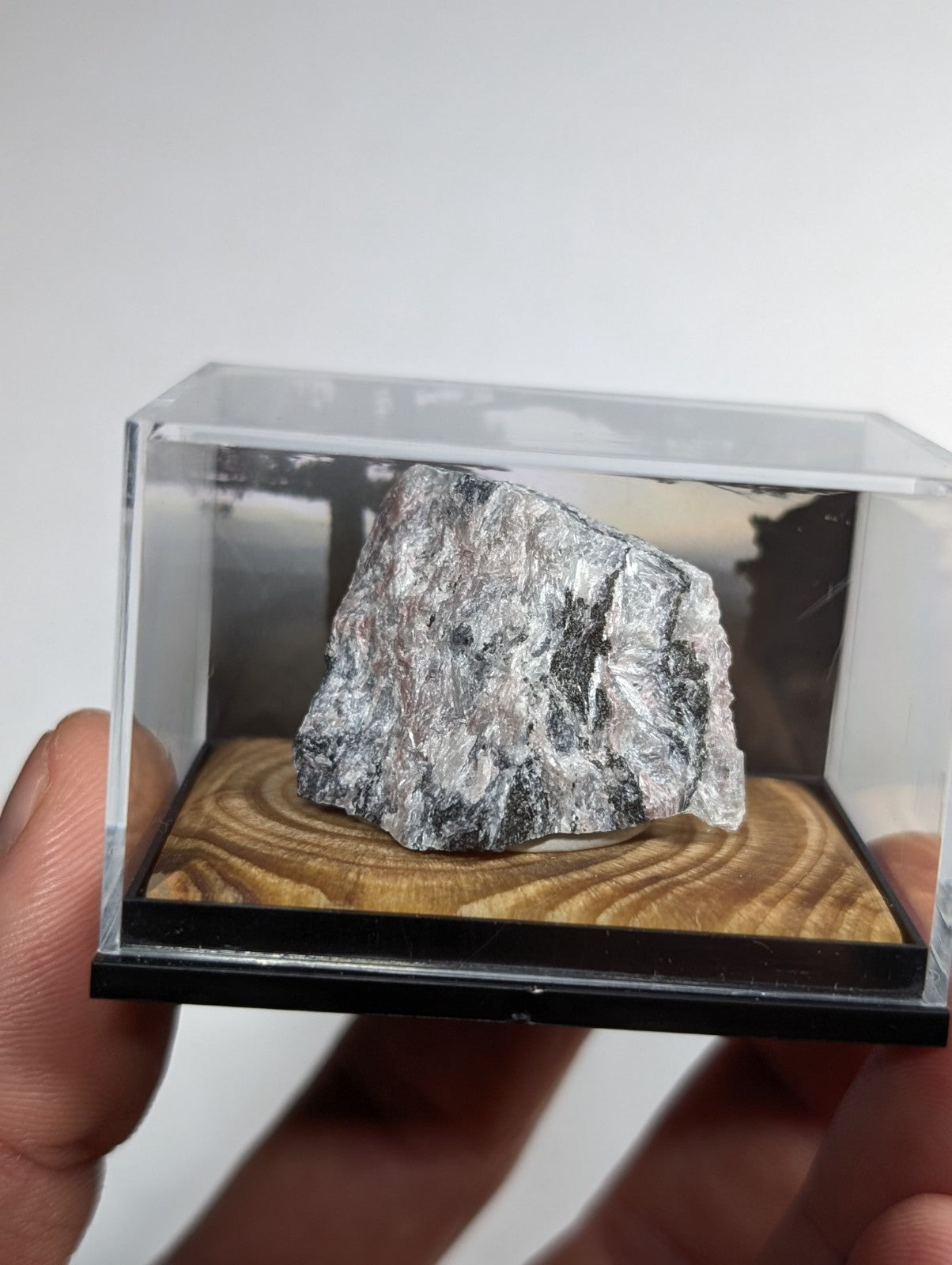 A silver-gray, rough-textured mineral specimen displayed in a clear acrylic display case.