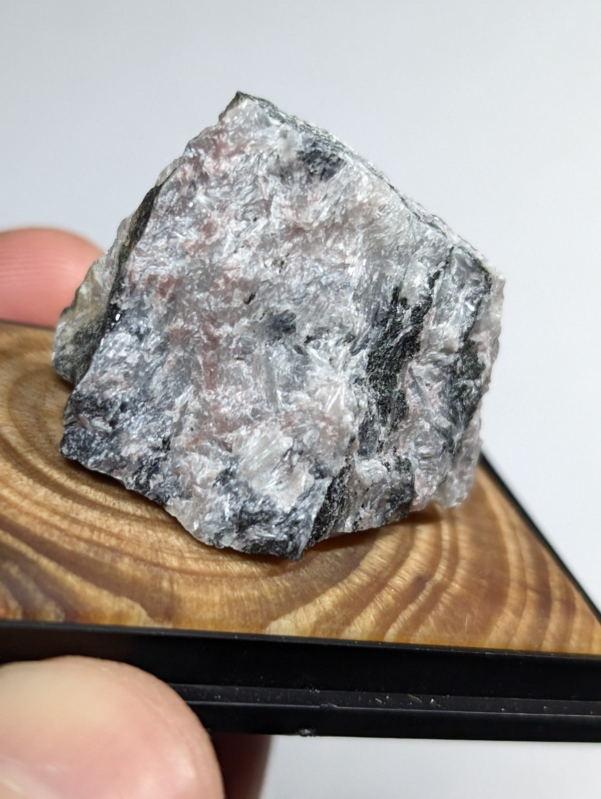 A rough, irregularly shaped mineral specimen with a mottled gray and white surface featuring subtle pinkish hues.