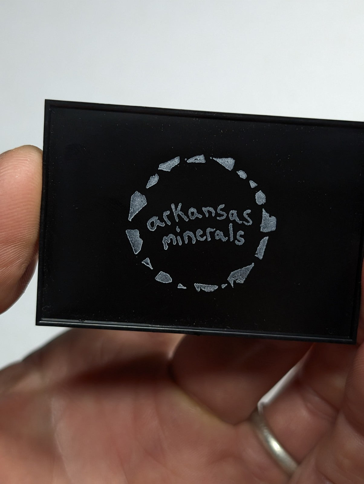 Black rectangular compact with silver engraved ’arkansas minerals’ logo surrounded by a circle of stylized mineral fragments.