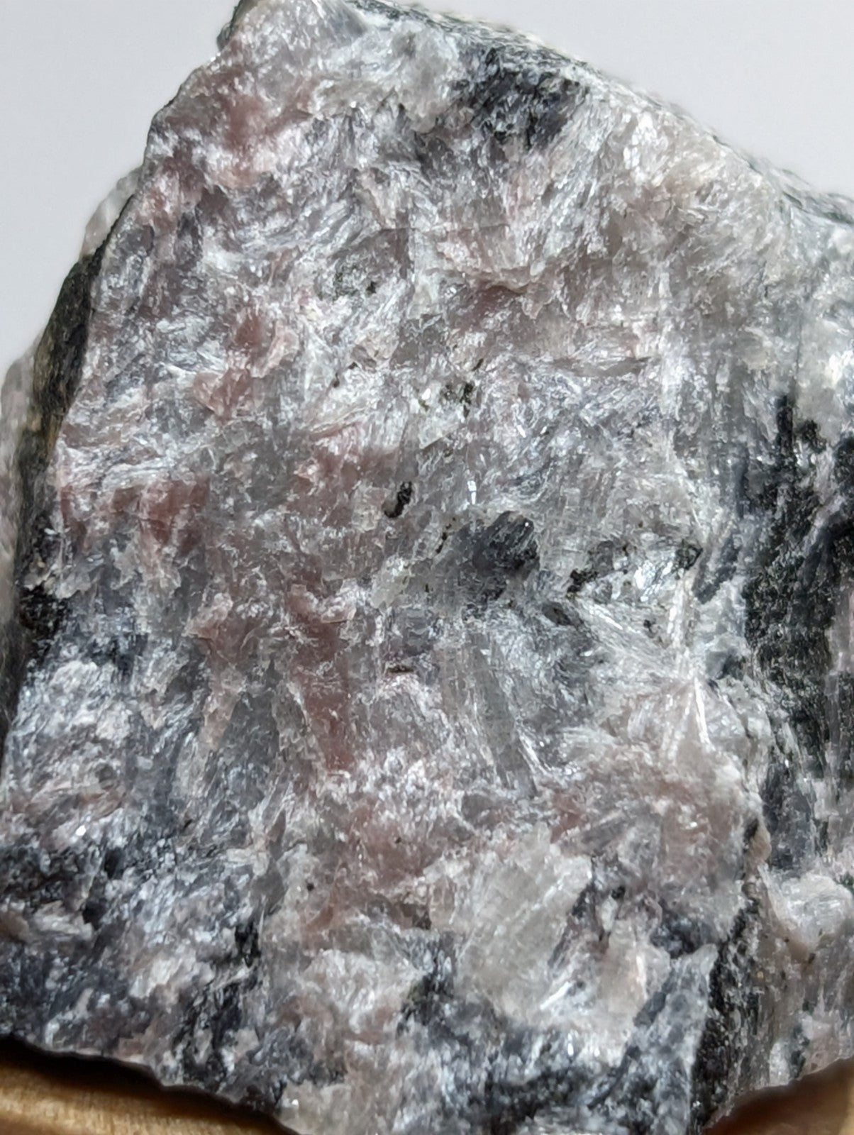 A rough, irregularly shaped mineral specimen with a mottled surface of gray, white, and faint pinkish hues.