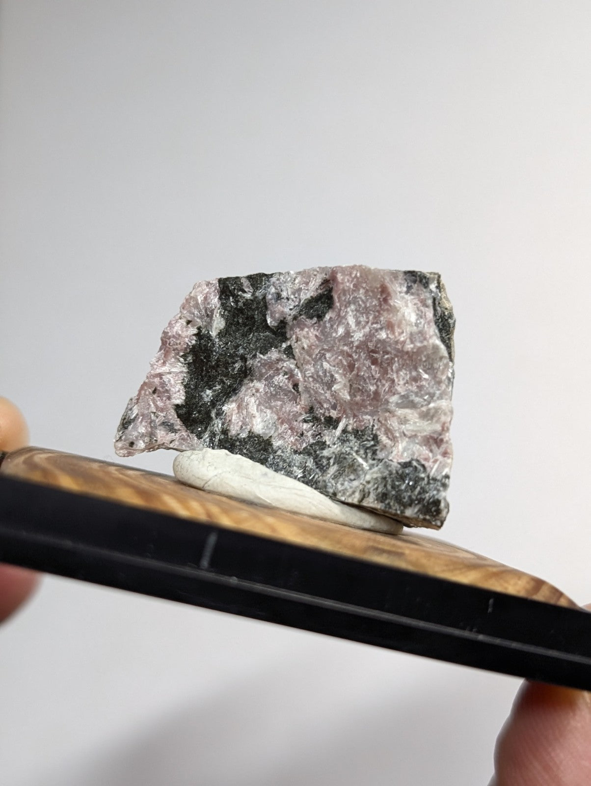 A rough, irregularly shaped mineral specimen with a mottled pattern of pinkish-purple and dark gray patches.