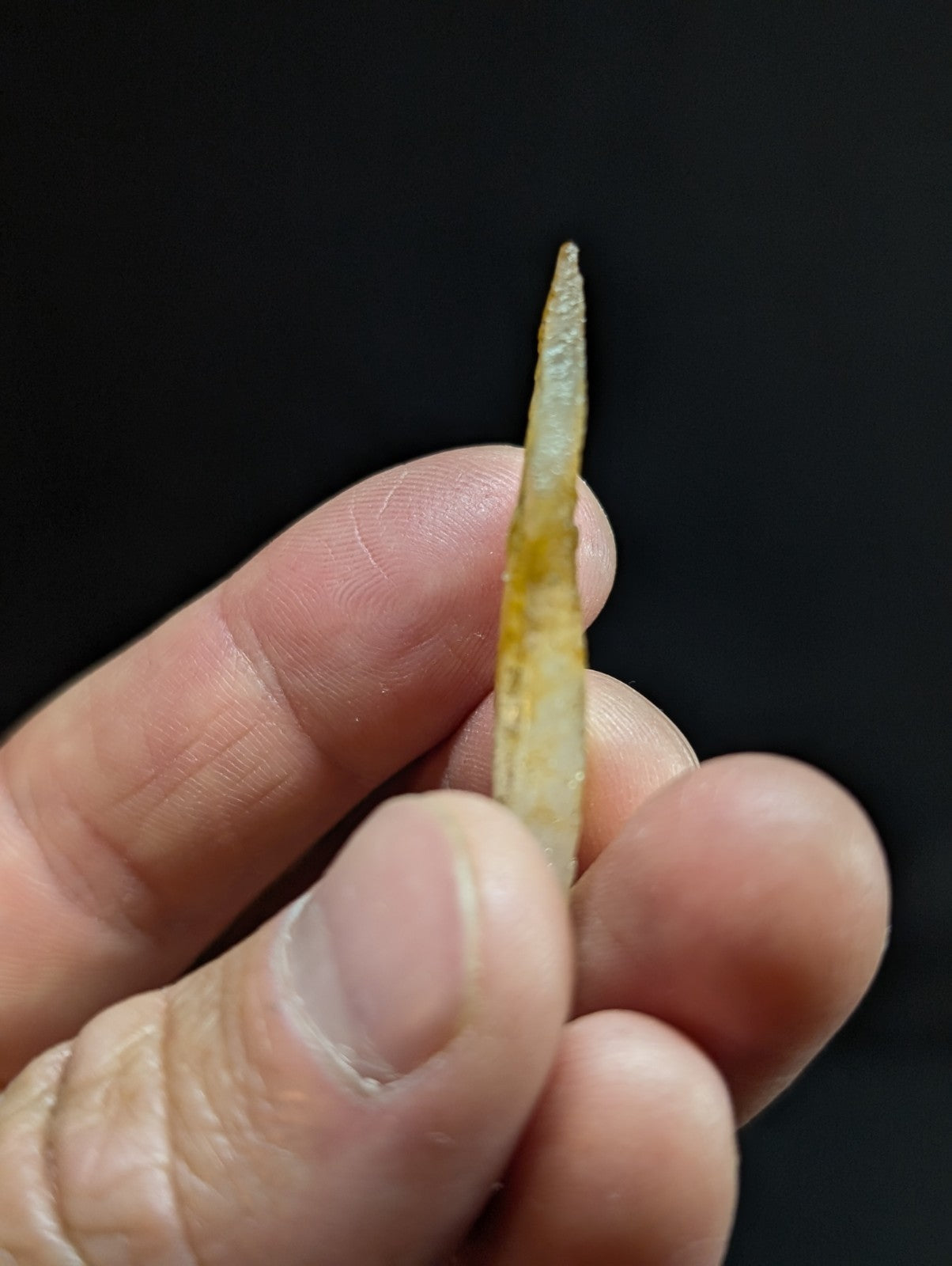 A translucent, pale yellowish-green stone arrowhead with a pointed tip and subtle striations along its length.