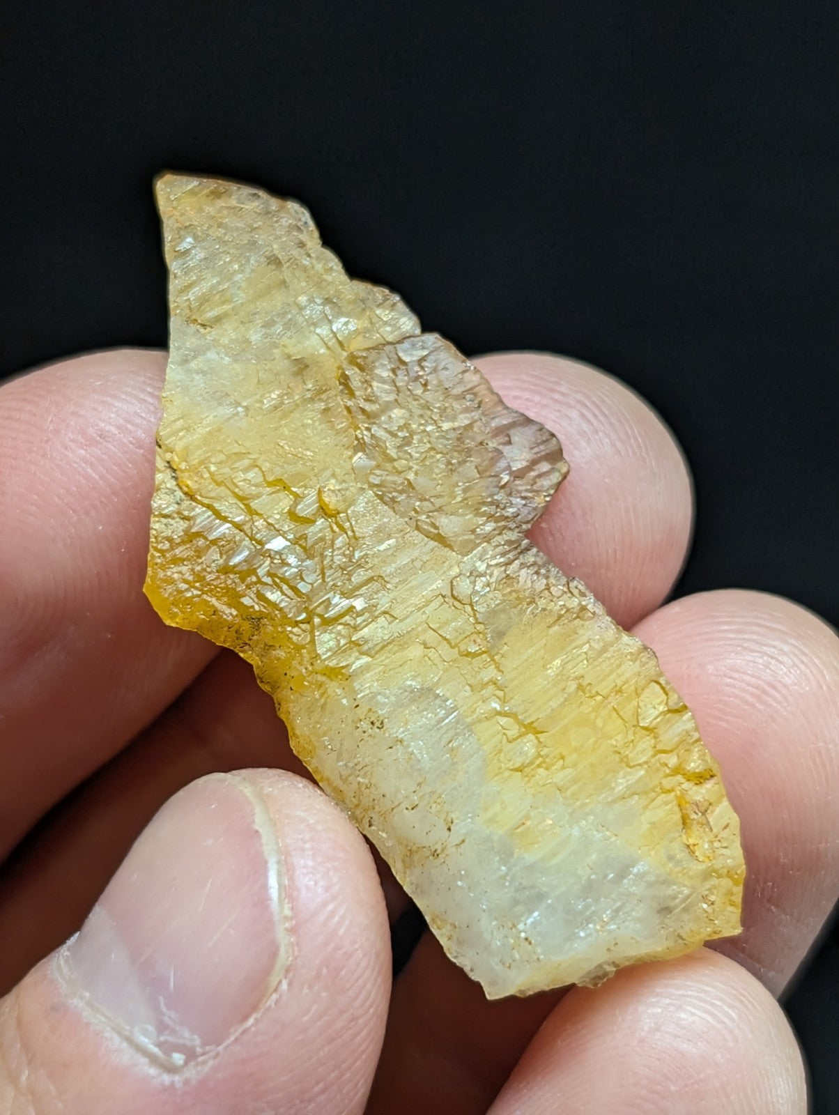 A translucent yellowish amber-colored mineral fragment with a rough, irregular surface and visible internal crystalline structures.