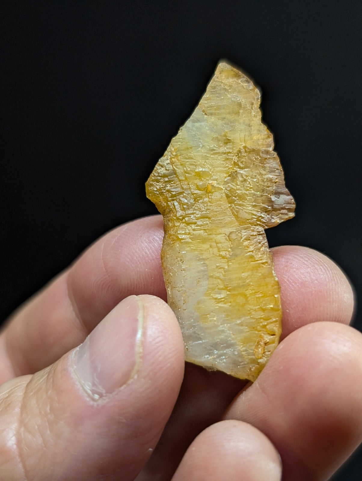 A translucent yellowish-green mineral specimen with a rough, irregularly shaped surface and visible internal crystalline patterns.
