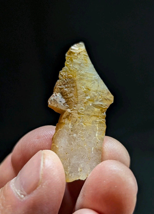 A translucent yellowish-green crystal fragment with a rough, jagged edge and visible internal striations.