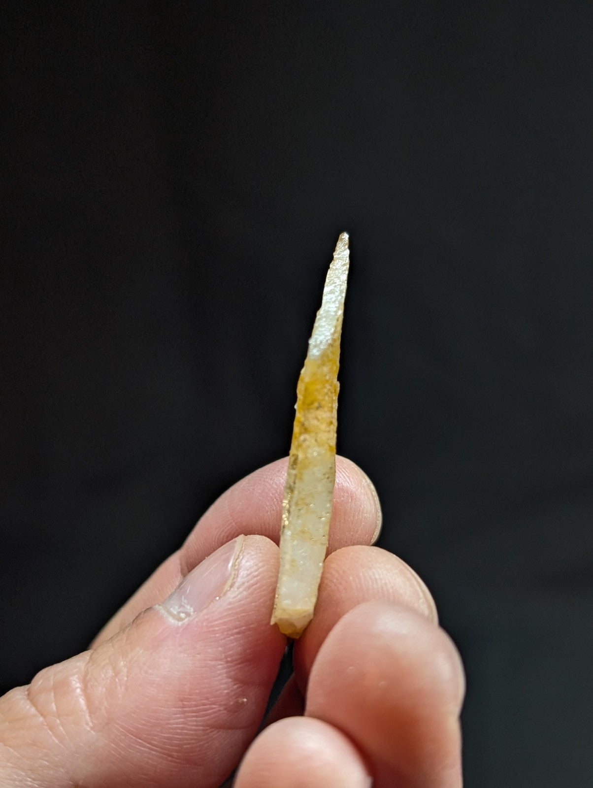 A slender, translucent jade dagger with a pointed tip and subtle yellowish-brown inclusions.