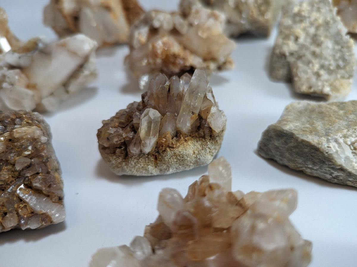 A cluster of translucent, amber-hued quartz crystals growing from a rough, earthy base.