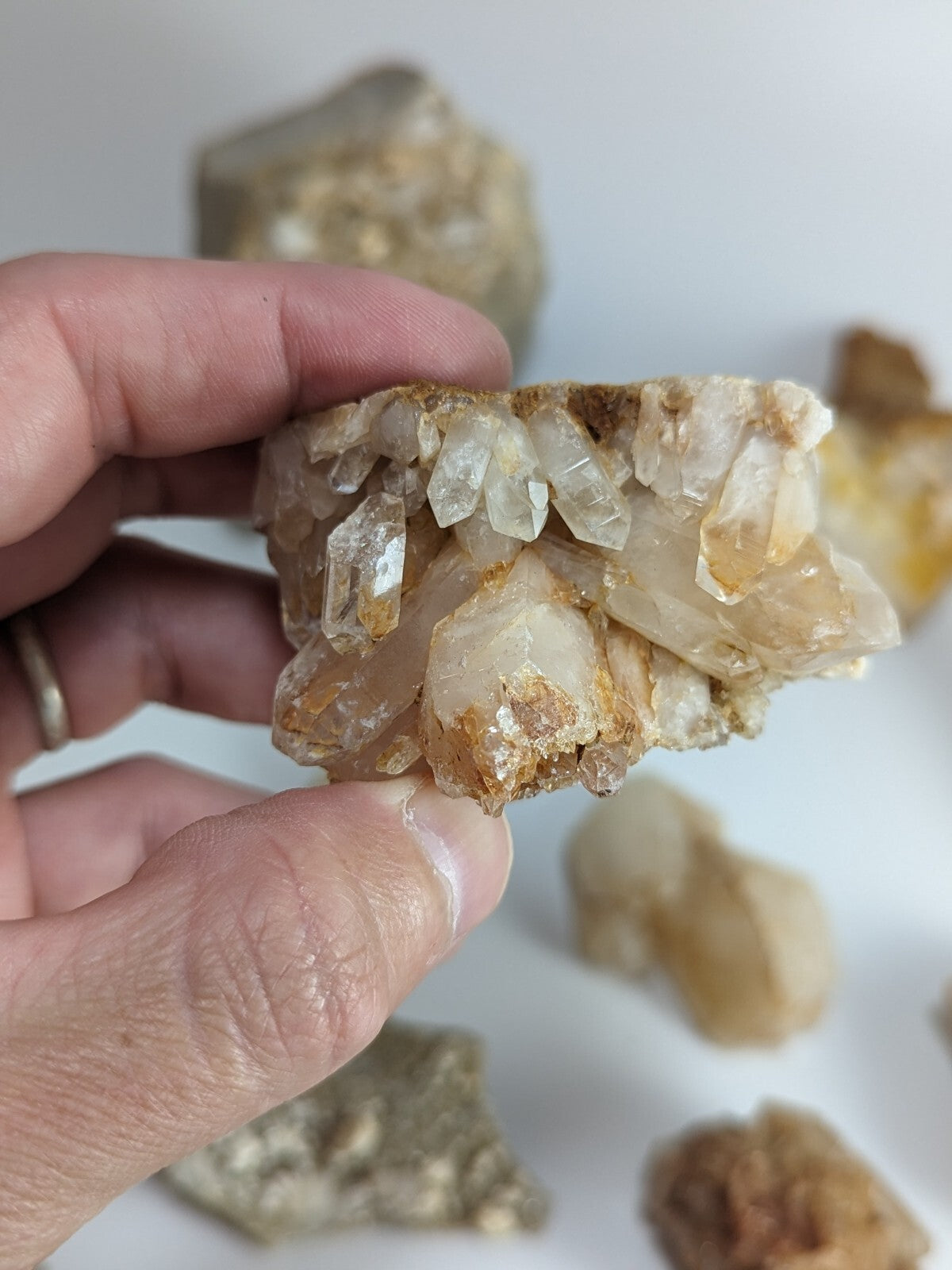 A hand holds a cluster of translucent, golden-hued quartz crystals with sharp, faceted edges and natural mineral inclusions.