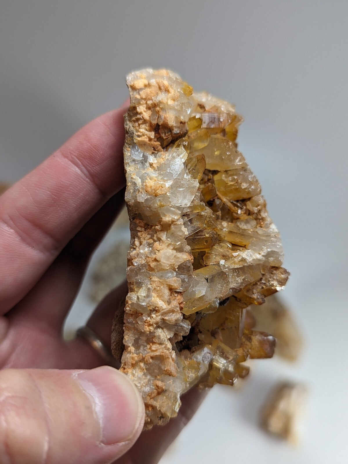 A hand holds a translucent amber-colored crystal cluster with clear, faceted crystals growing from a rougher, earthy brown matrix.