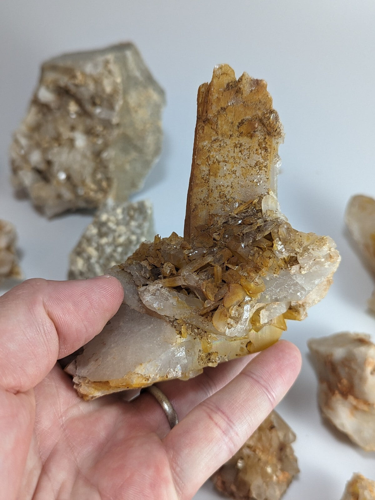A hand holds a translucent quartz crystal formation with golden-yellow inclusions and sharp, faceted edges.