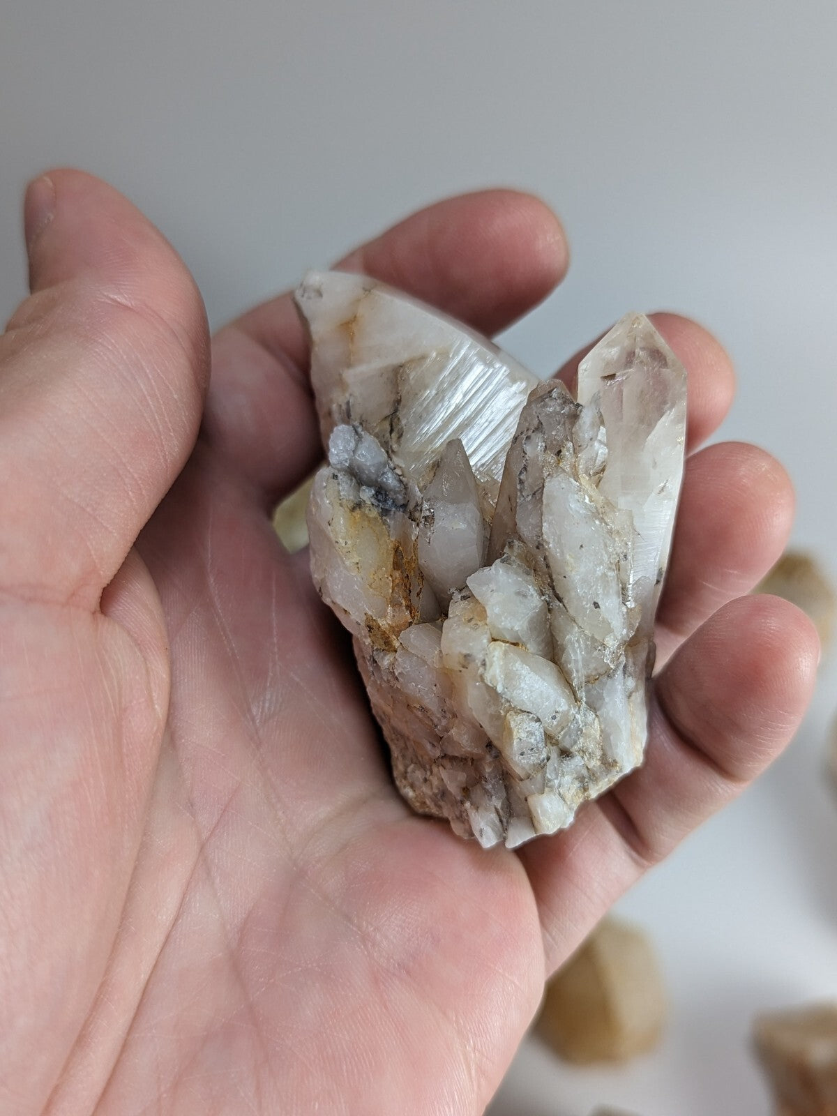 A translucent white quartz crystal cluster with natural facets and subtle golden inclusions, held gently in a hand.