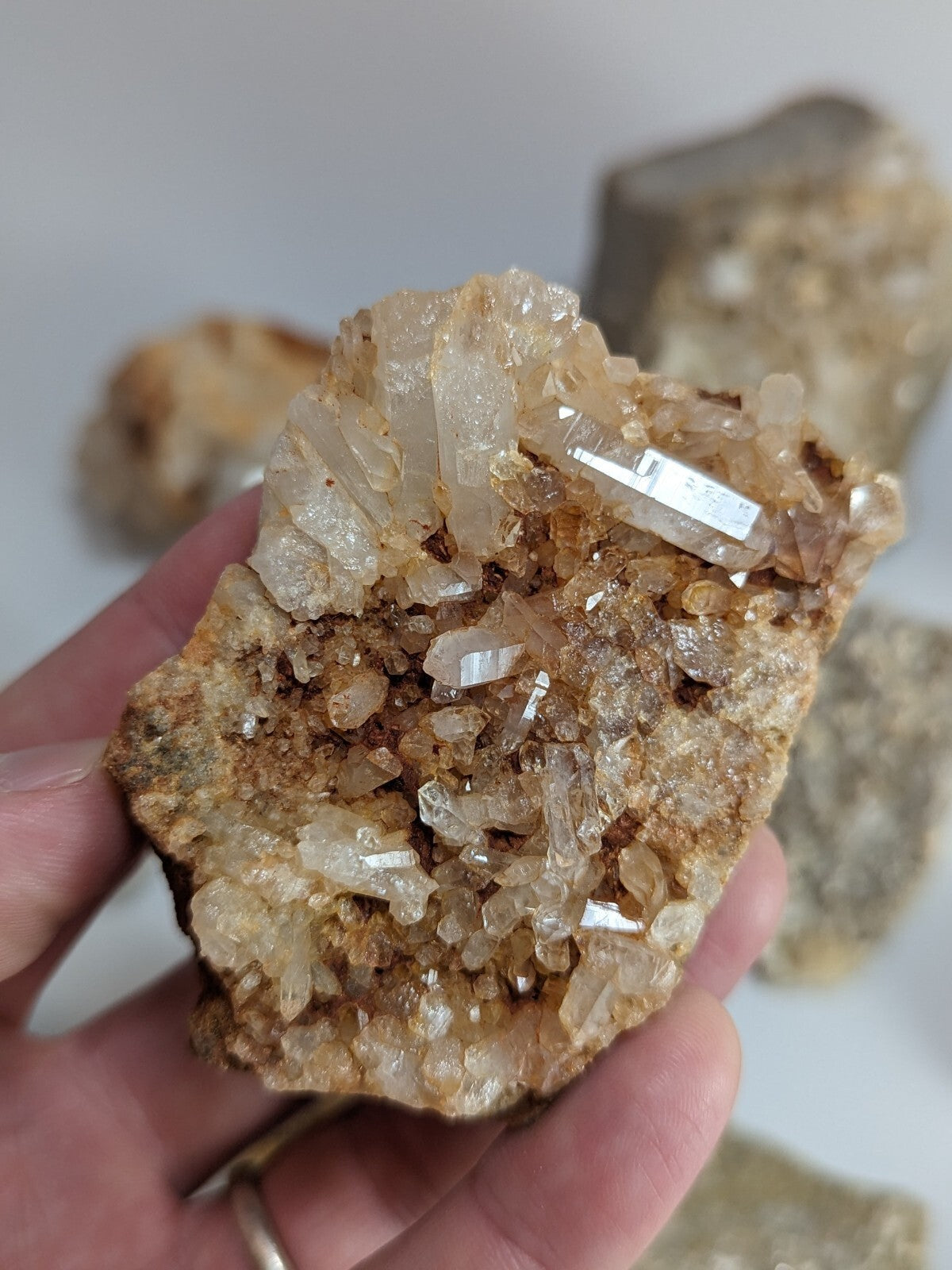 A hand holds a translucent, crystalline quartz geode with golden-brown matrix and clear, faceted crystal formations.