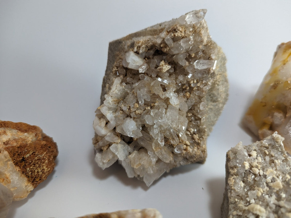 A translucent quartz crystal cluster growing from a rough, earthy matrix with clear facets and subtle golden inclusions.