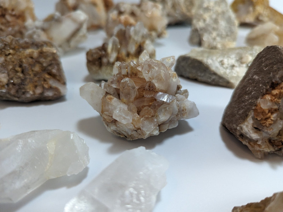 A cluster of translucent, faceted quartz crystals with a warm amber hue nestled within a rougher brown matrix.