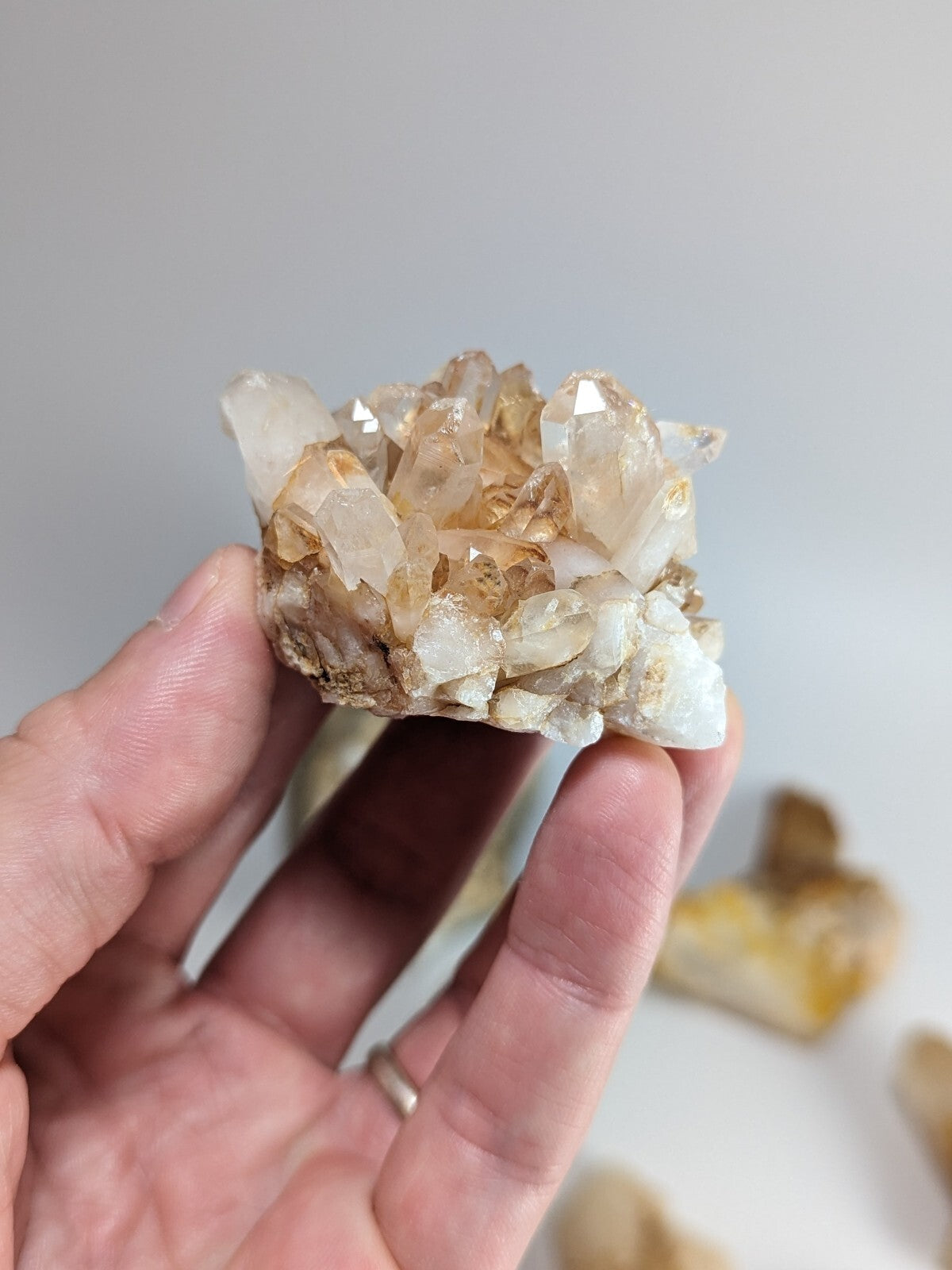 A hand holds a cluster of translucent, golden-hued quartz crystals with sharp, faceted points and natural mineral formations.