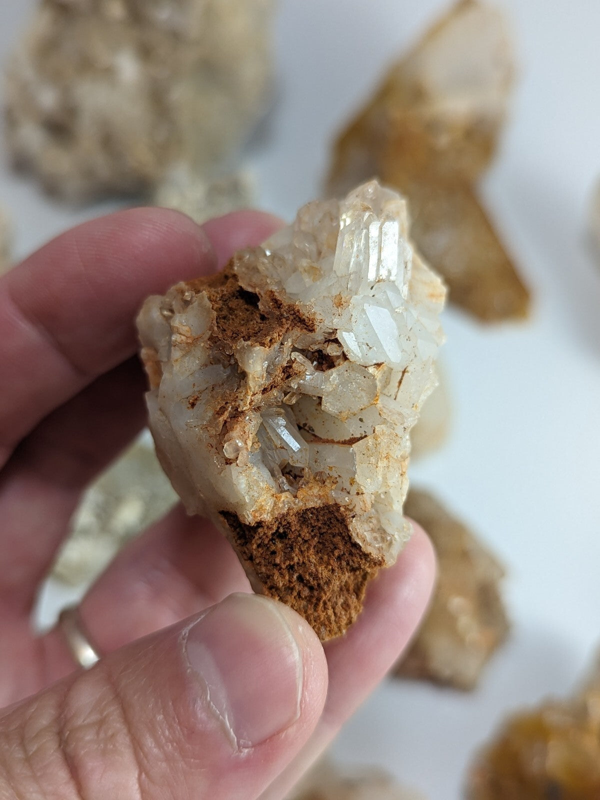 A hand holds a cluster of translucent, crystalline quartz with golden-brown matrix.