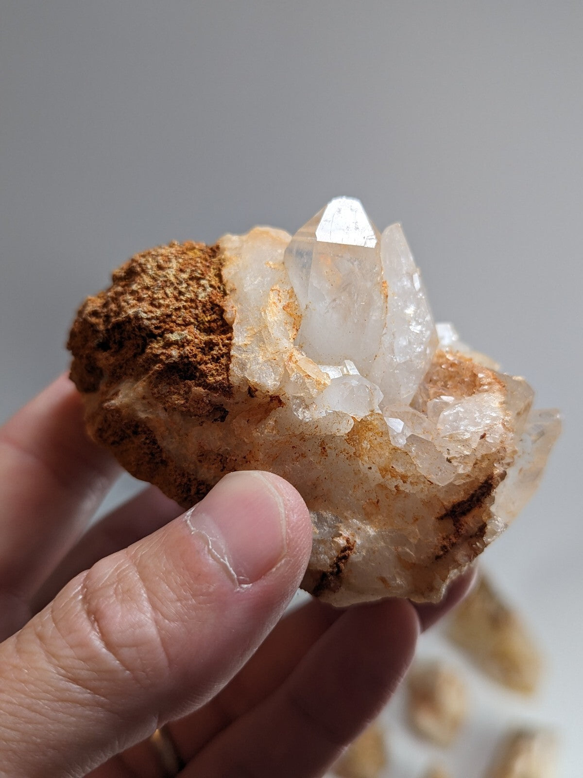 A hand holds a clear quartz crystal cluster with golden-brown matrix rock.