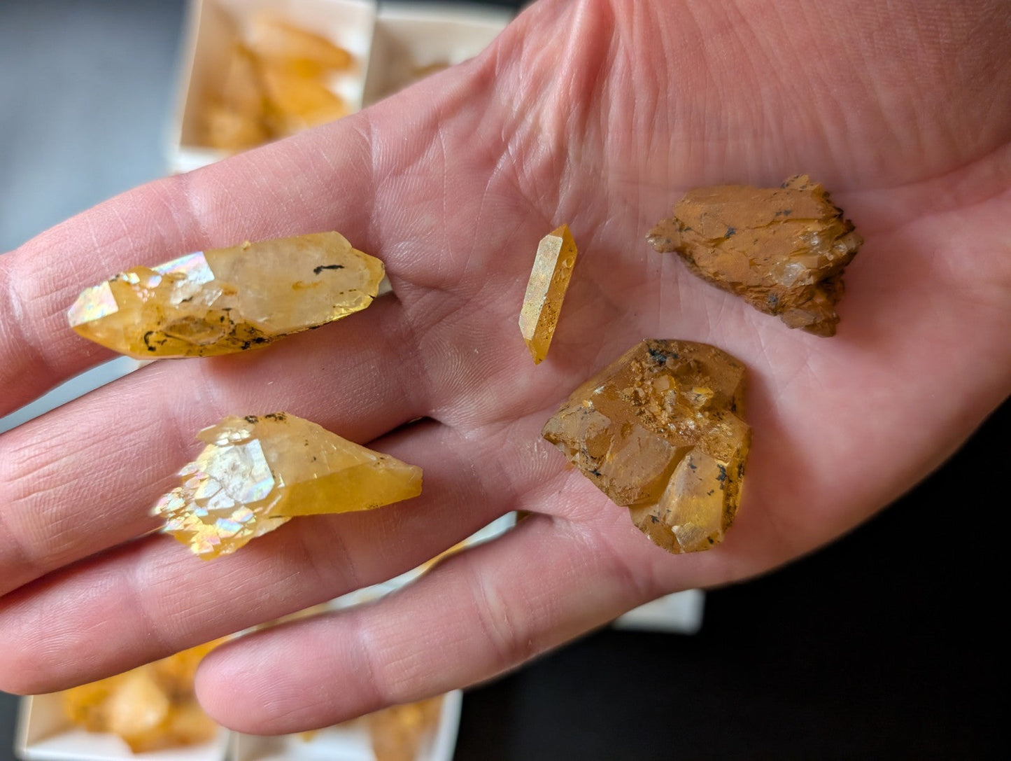 A hand holds several translucent yellow-orange citrine crystals, some with visible inclusions and rough edges.