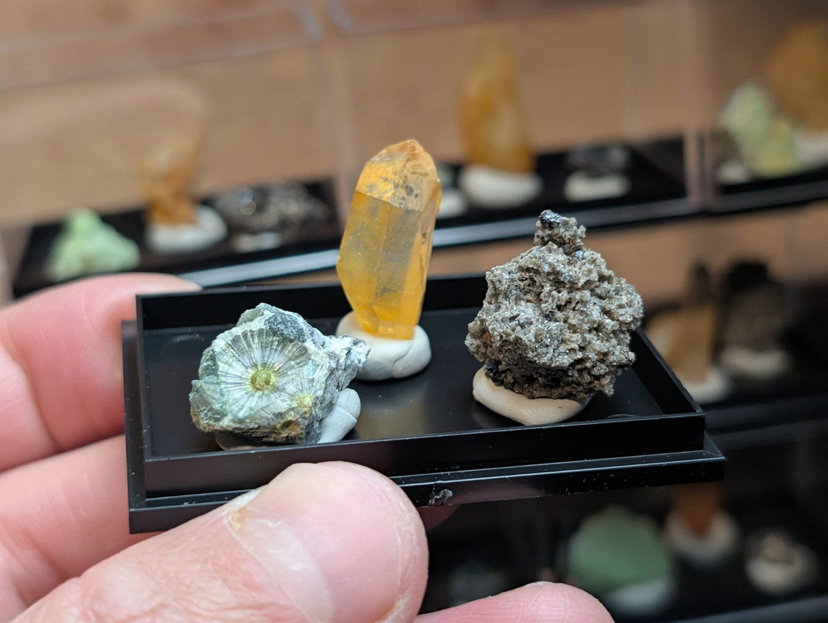 A yellow-orange crystal specimen with a translucent, faceted appearance sits on a white pedestal within a black display tray.