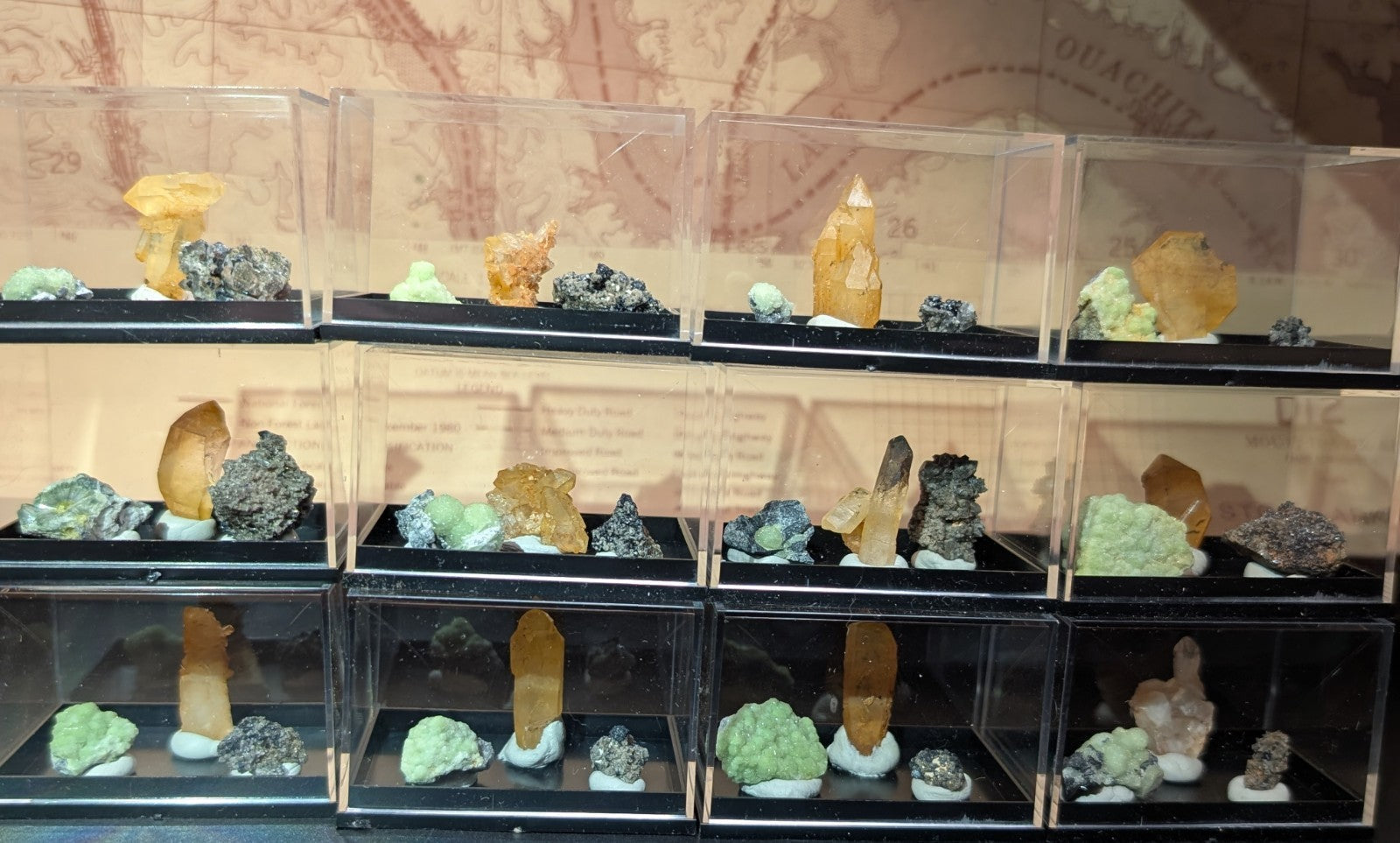 A collection of mineral specimens in clear display cases, featuring vibrant yellow and green crystals alongside dark metallic ores.