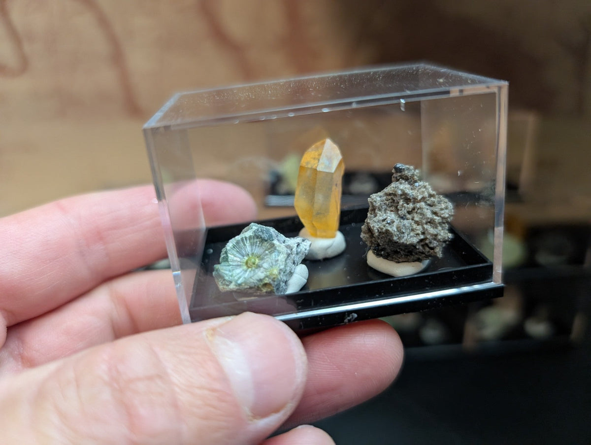 Clear acrylic display case holding three mineral specimens on a black base.
