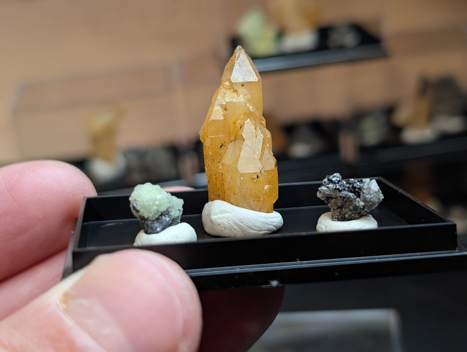 A tall, translucent yellow crystal with a pointed tip and visible facets sits prominently in the center of a black display tray.