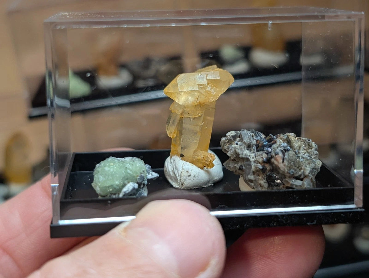 A translucent yellow crystal with a faceted, geometric structure sits prominently in the center of a clear acrylic display case.