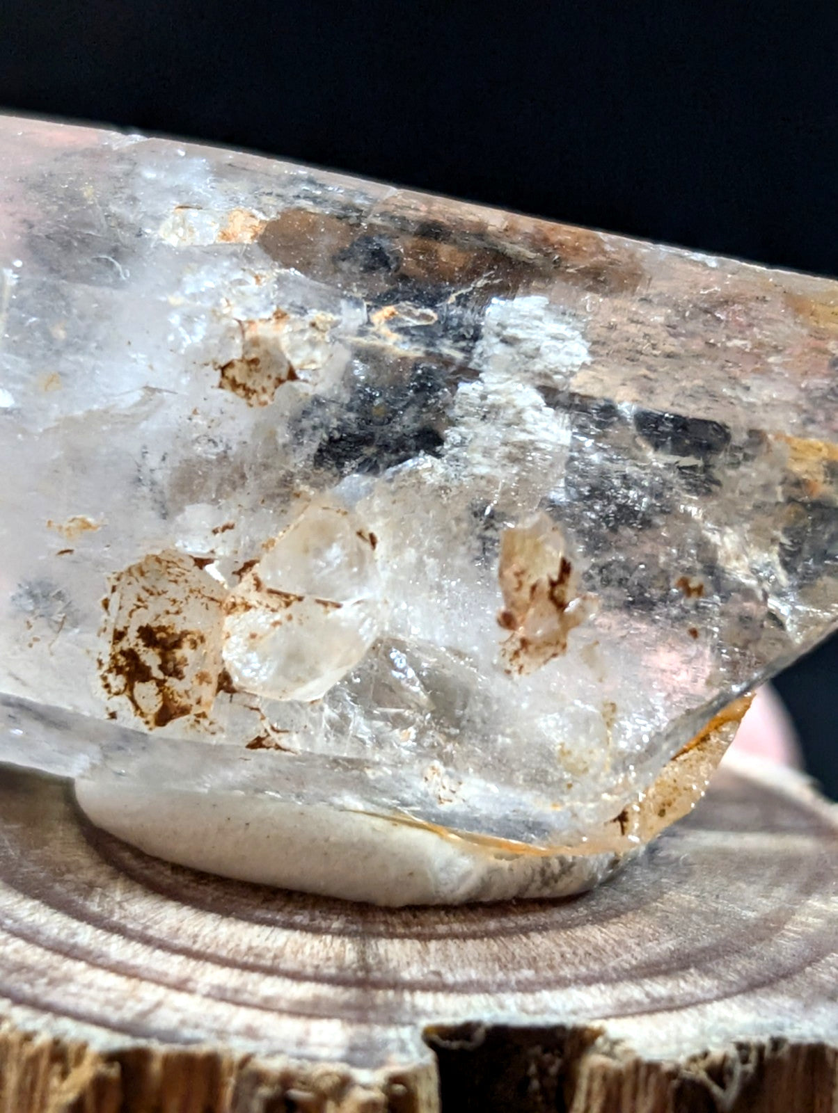 A translucent quartz crystal with natural inclusions and earthy brown veining, resting on a wooden surface.