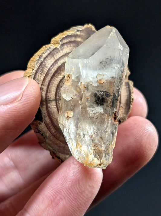 A translucent, clear quartz crystal with natural inclusions and a rough, earthy base.