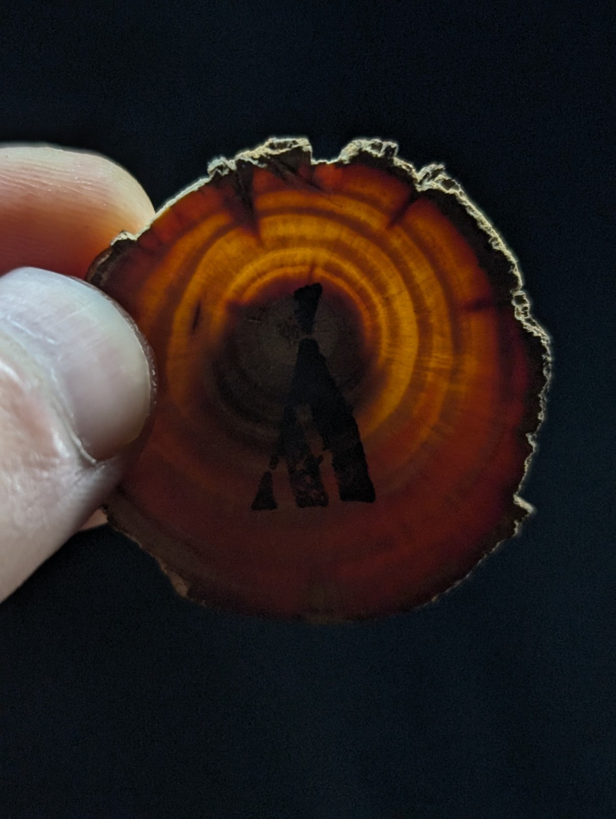 A circular, amber-hued agate slice with concentric rings and a dark silhouette of a figure etched into its center.