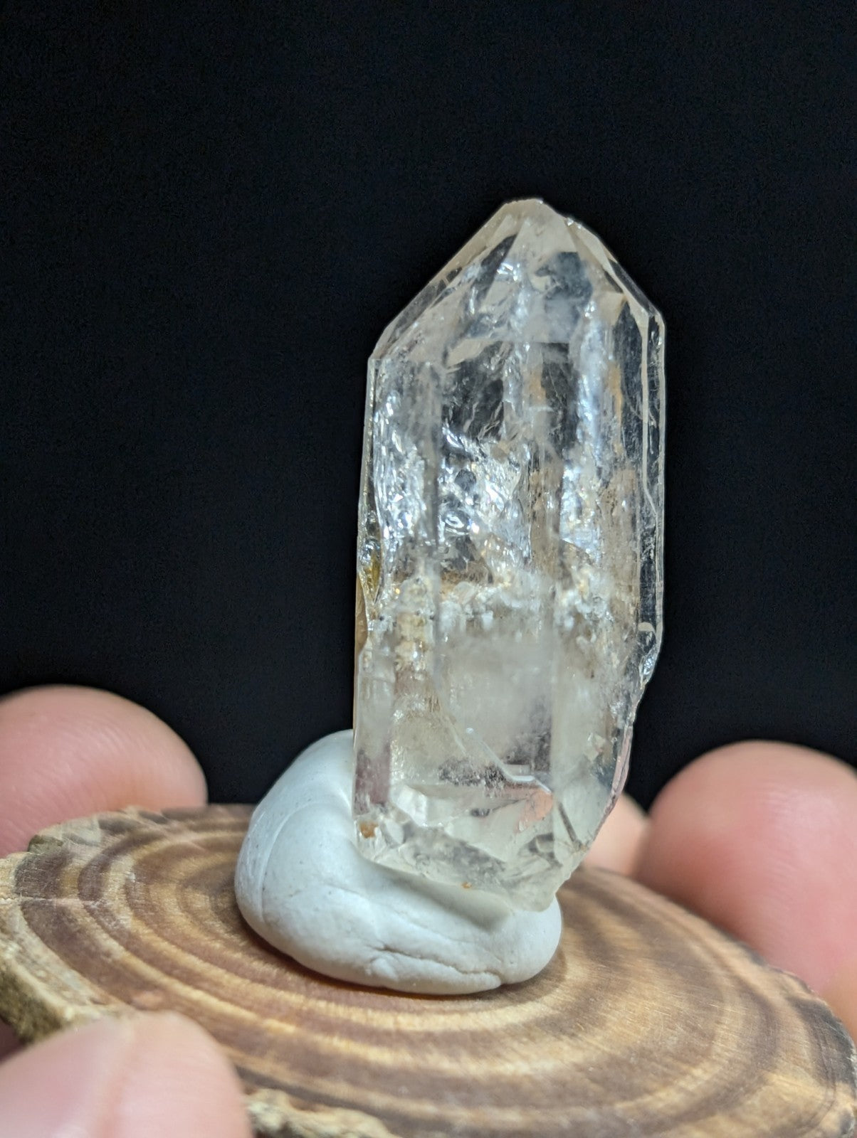 A clear, faceted quartz crystal with natural inclusions and a pointed tip, displayed on a light gray stone base.