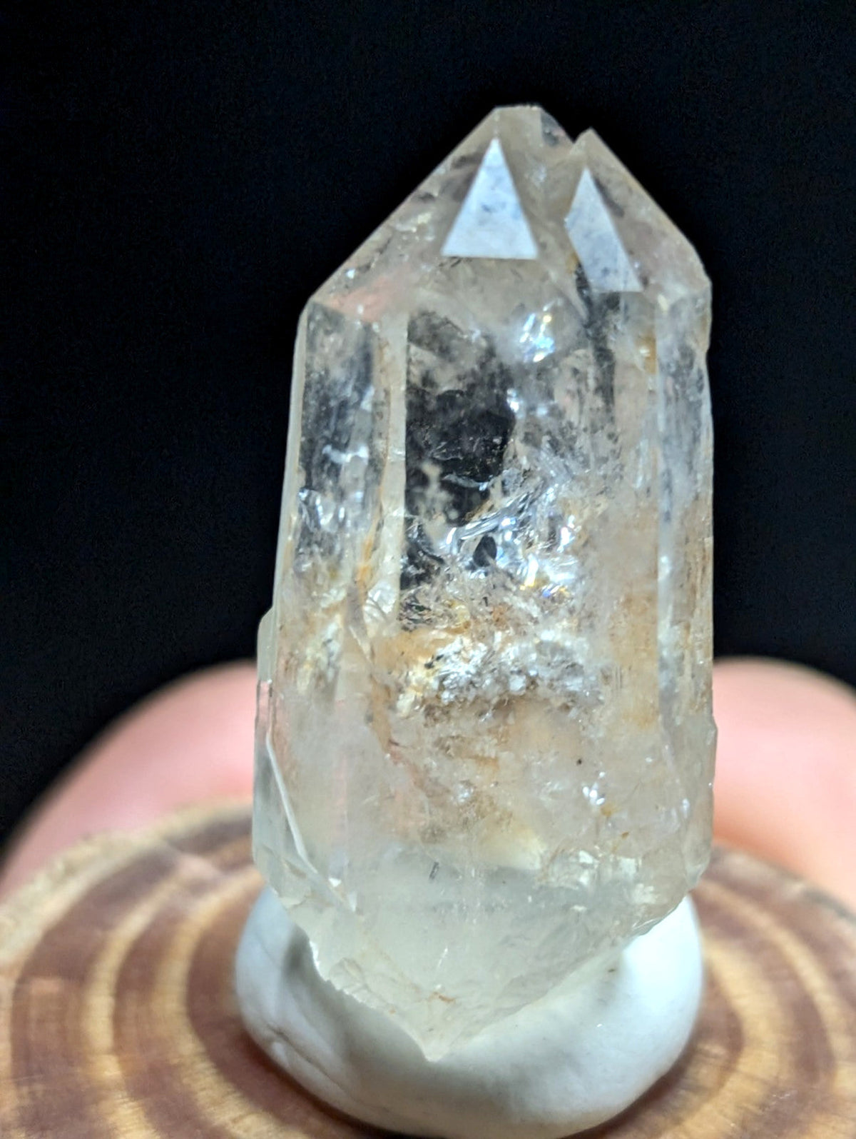 A clear, translucent quartz crystal with a pointed top and natural inclusions sits on a white pedestal.