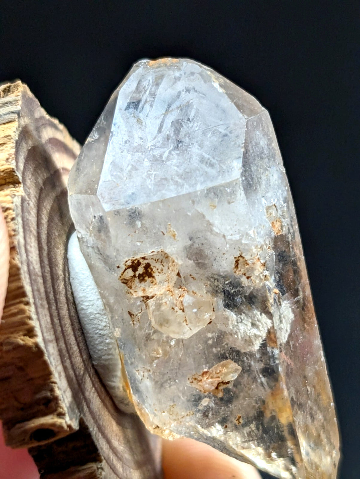 A translucent, clear quartz crystal with natural inclusions and earthy brownish mineral deposits embedded within its structure.
