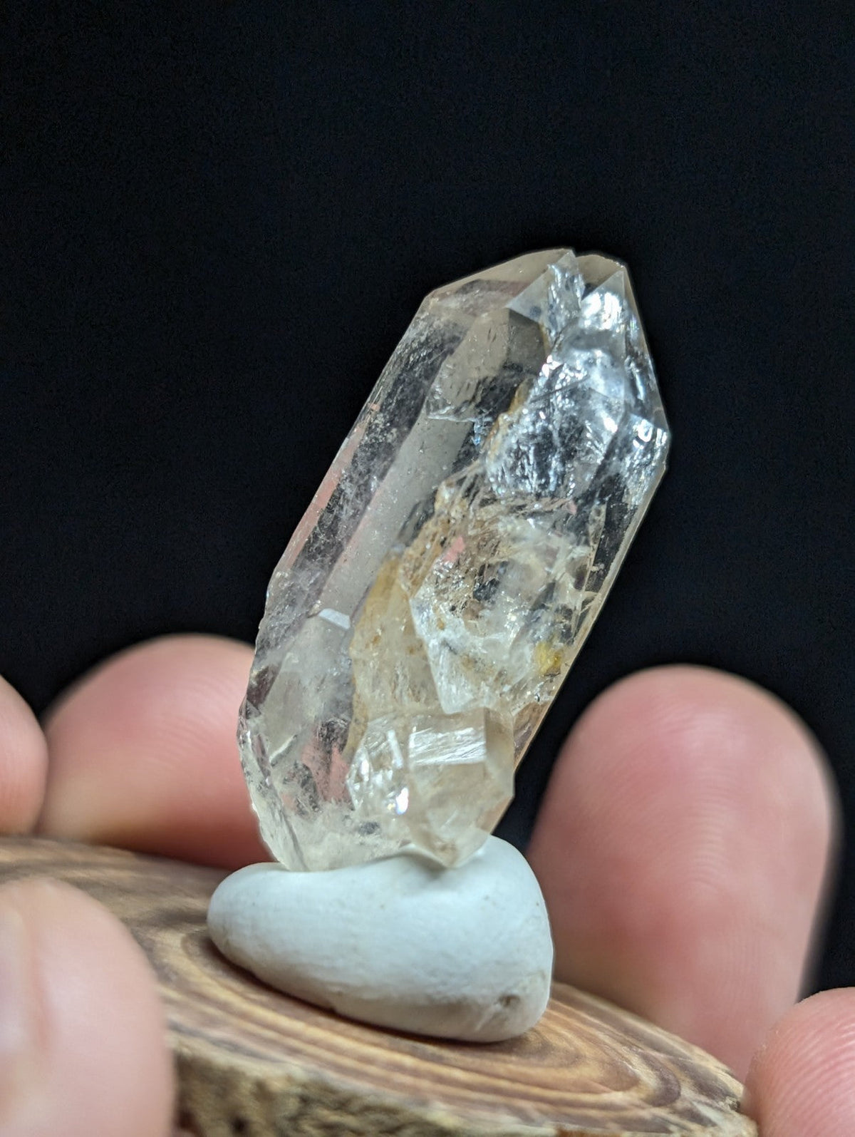 A clear, faceted quartz crystal with subtle yellowish inclusions stands upright on a smooth white stone base.