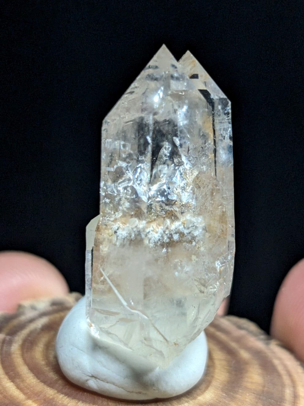 A clear, translucent quartz crystal with a pointed top and natural internal inclusions sits on a white stone base.