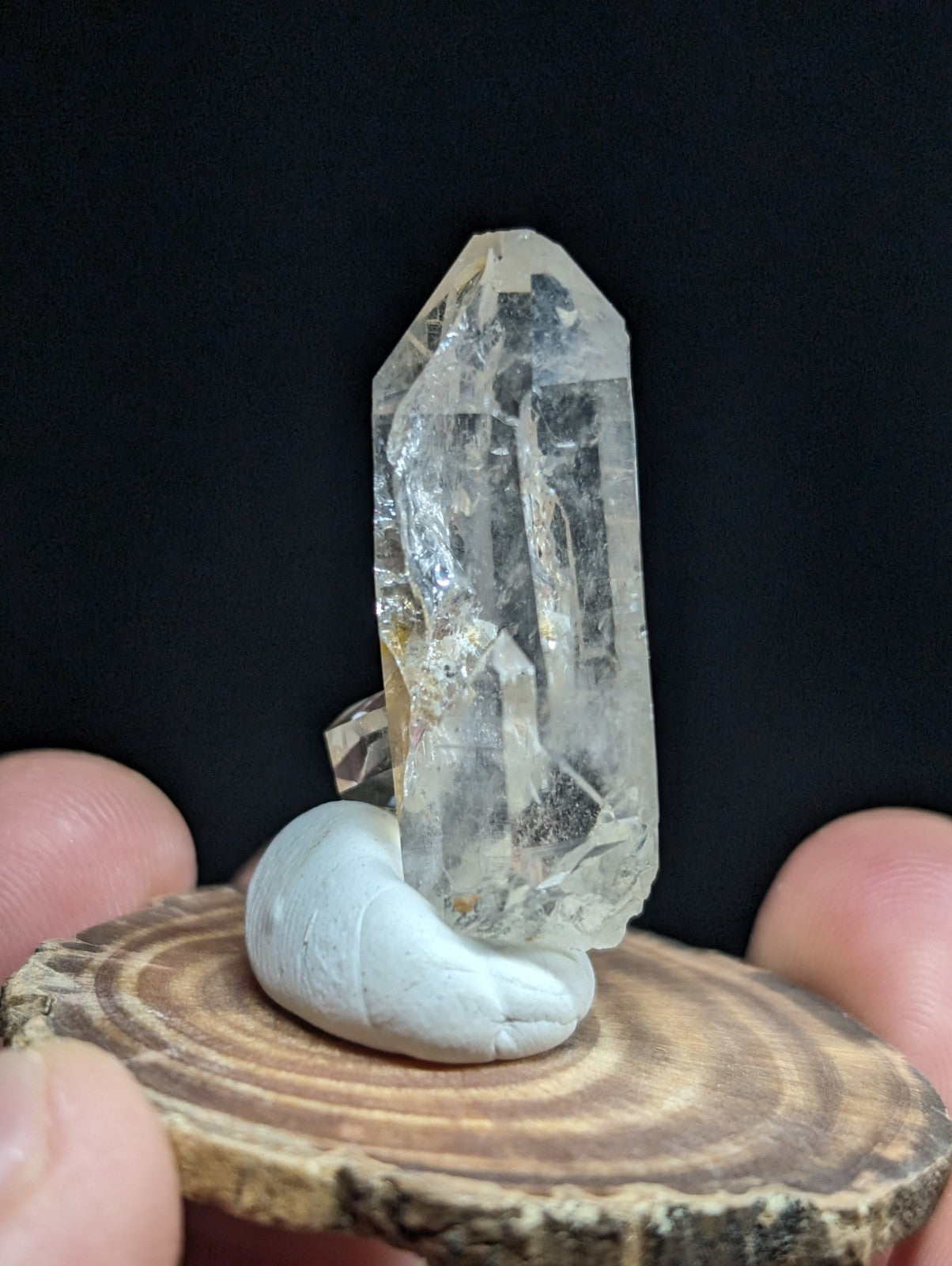 A clear, translucent quartz crystal with natural inclusions and facets stands upright on a smooth white stone base.