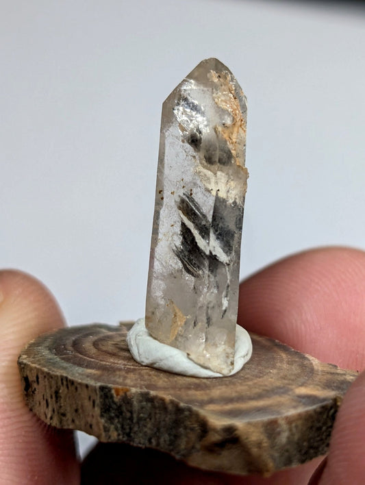 A translucent quartz crystal with natural inclusions and a pointed tip, mounted on a circular wooden base.