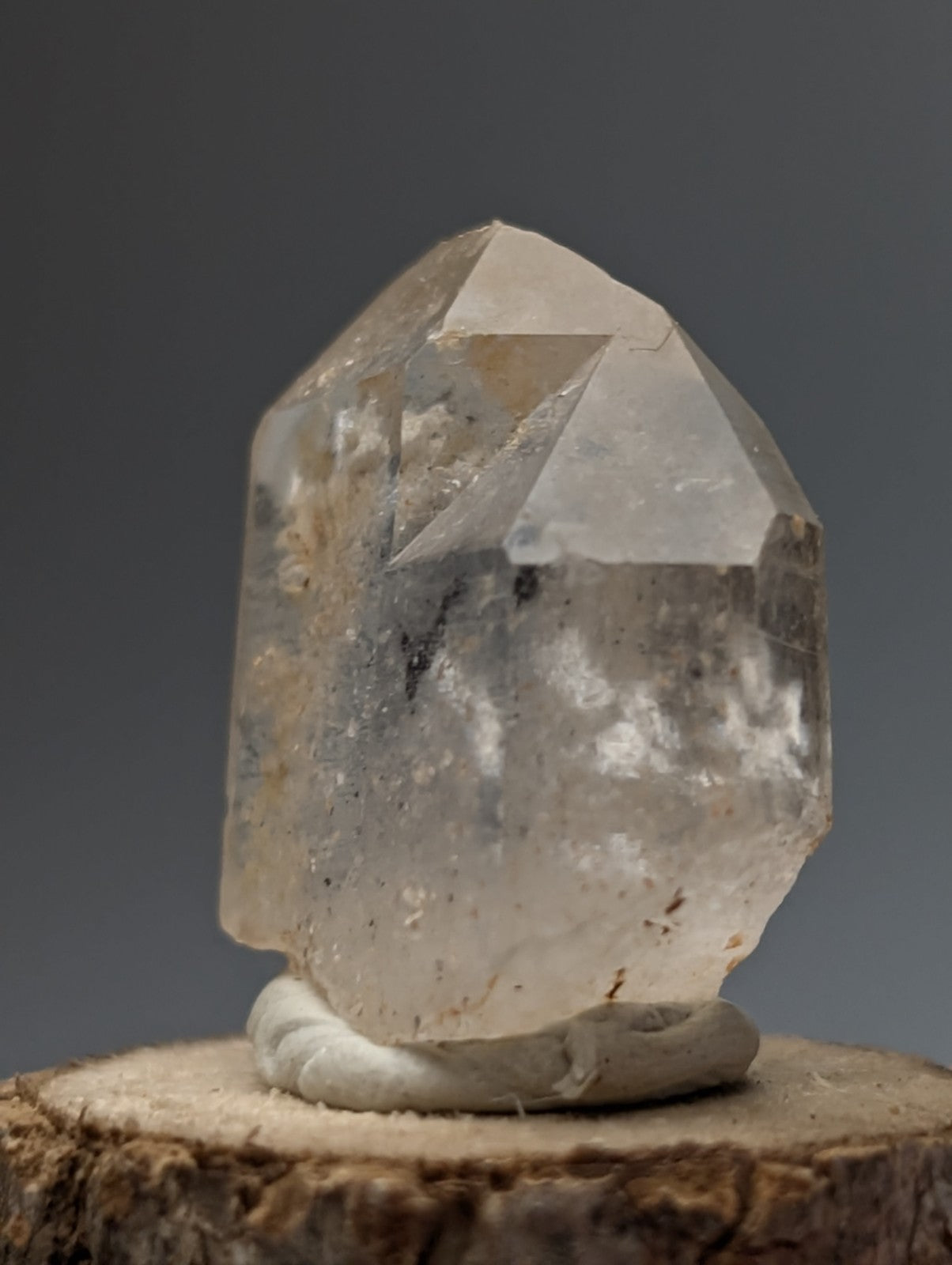 A translucent clear quartz crystal point with nacrite and manganese inclusions from arkansas on a wood base