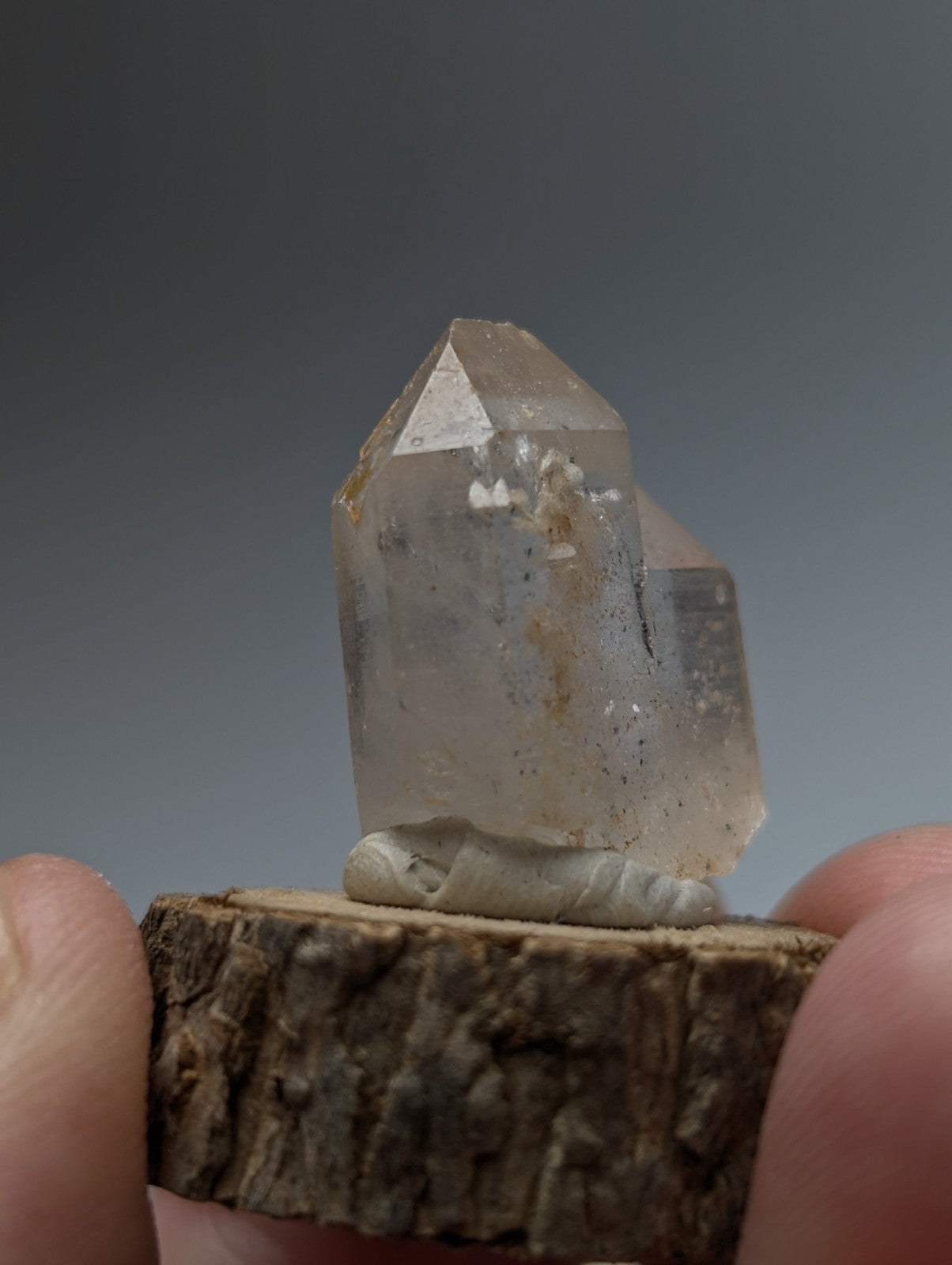 Translucent clear quartz crystal point with nacrite and manganese inclusions on rustic wood base from arkansas