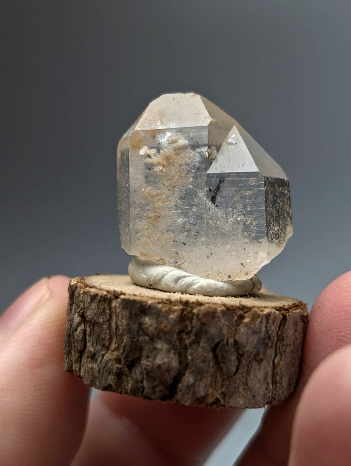 A clear faceted quartz crystal point with nacrite and manganese inclusions on a wood base from arkansas