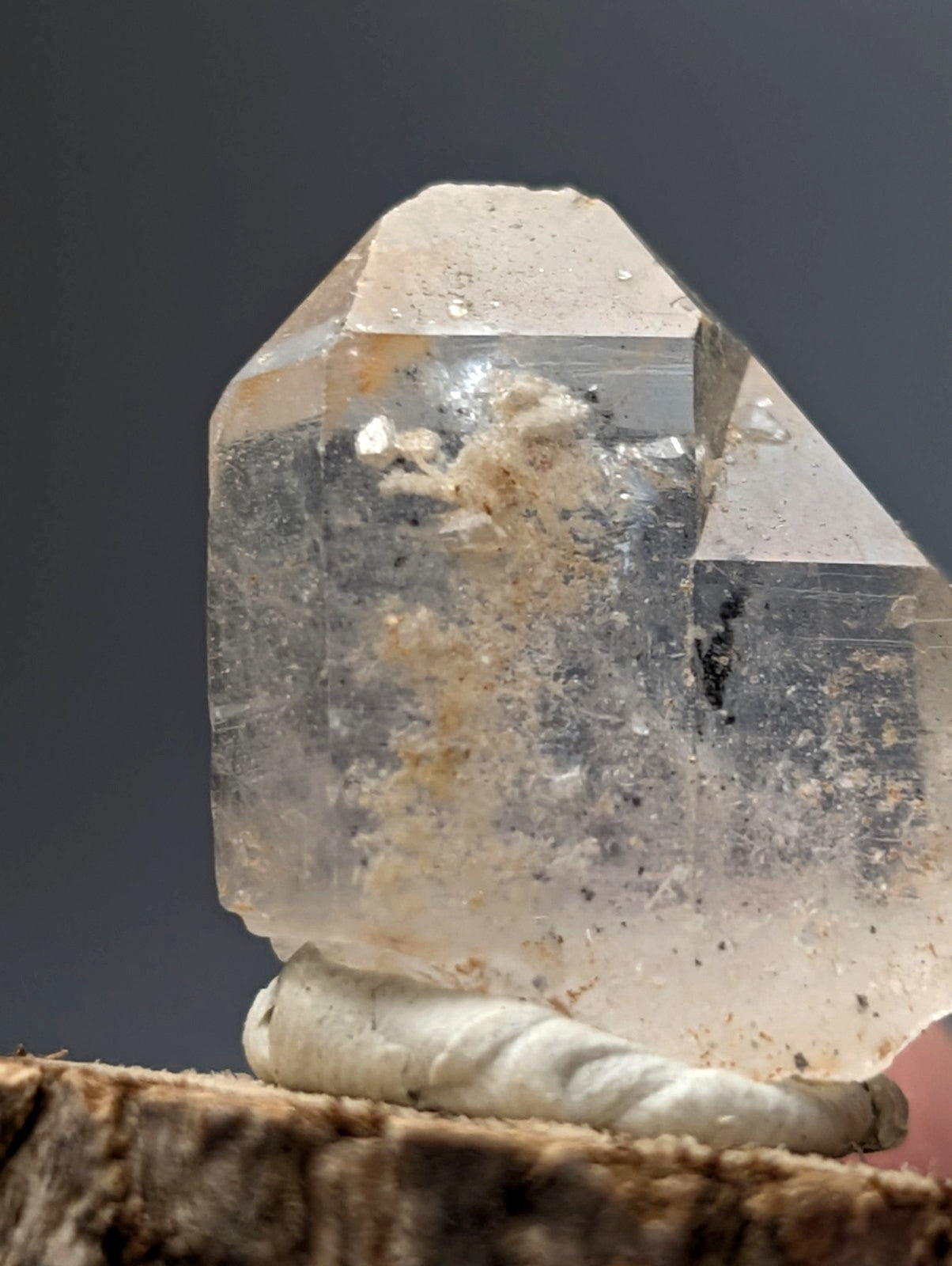 Translucent quartz crystal point with nacrite and manganese inclusions resting on a wooden base from Arkansas