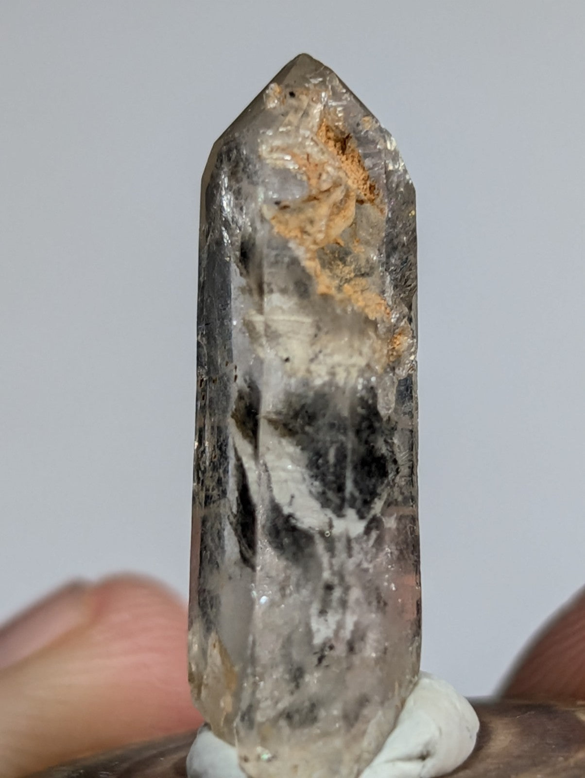 A translucent, grayish quartz crystal with natural inclusions and a pointed tip.