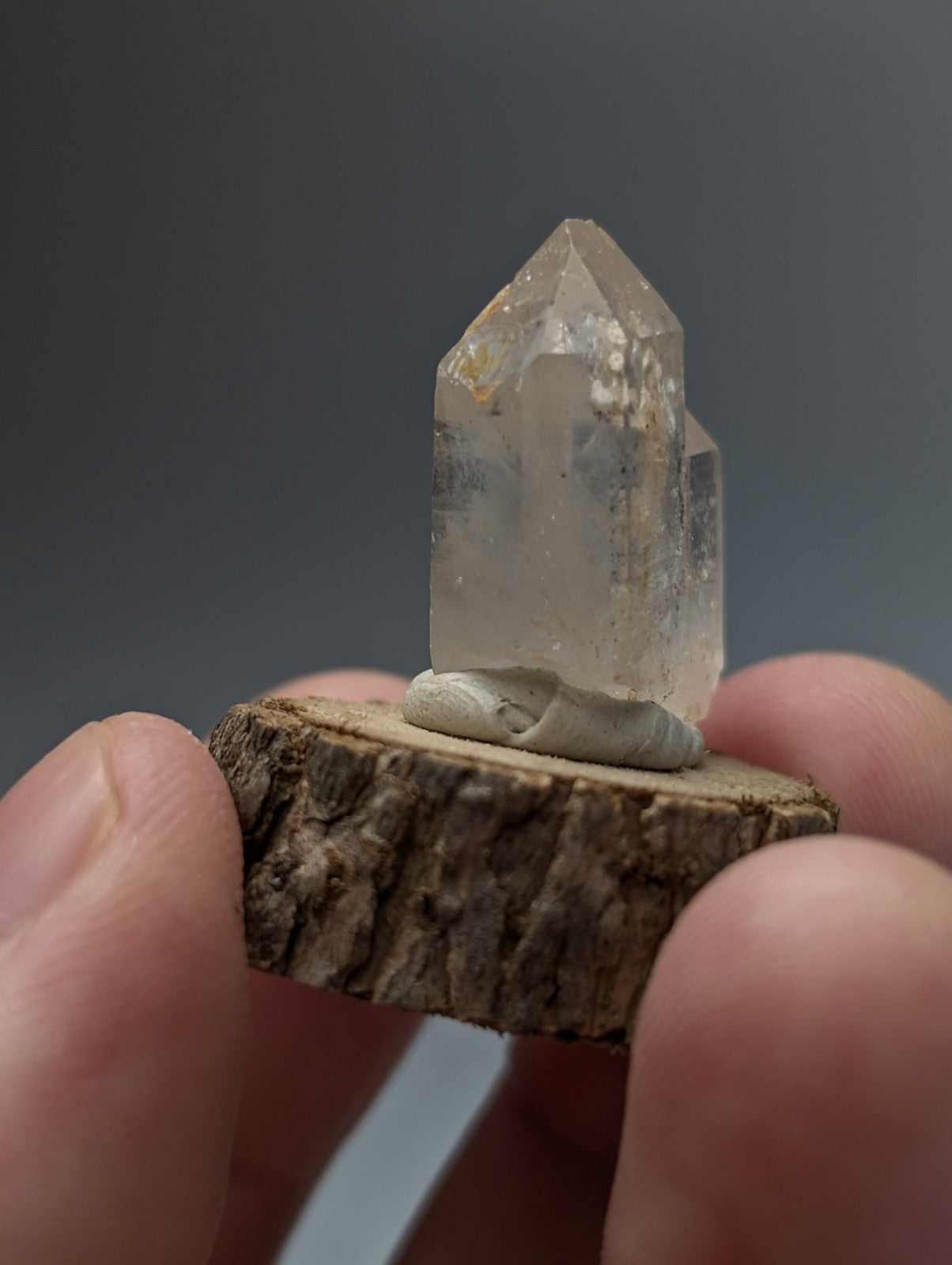 A nacrite and manganese included clear quartz crystal point with natural inclusions mounted on a rustic wood base