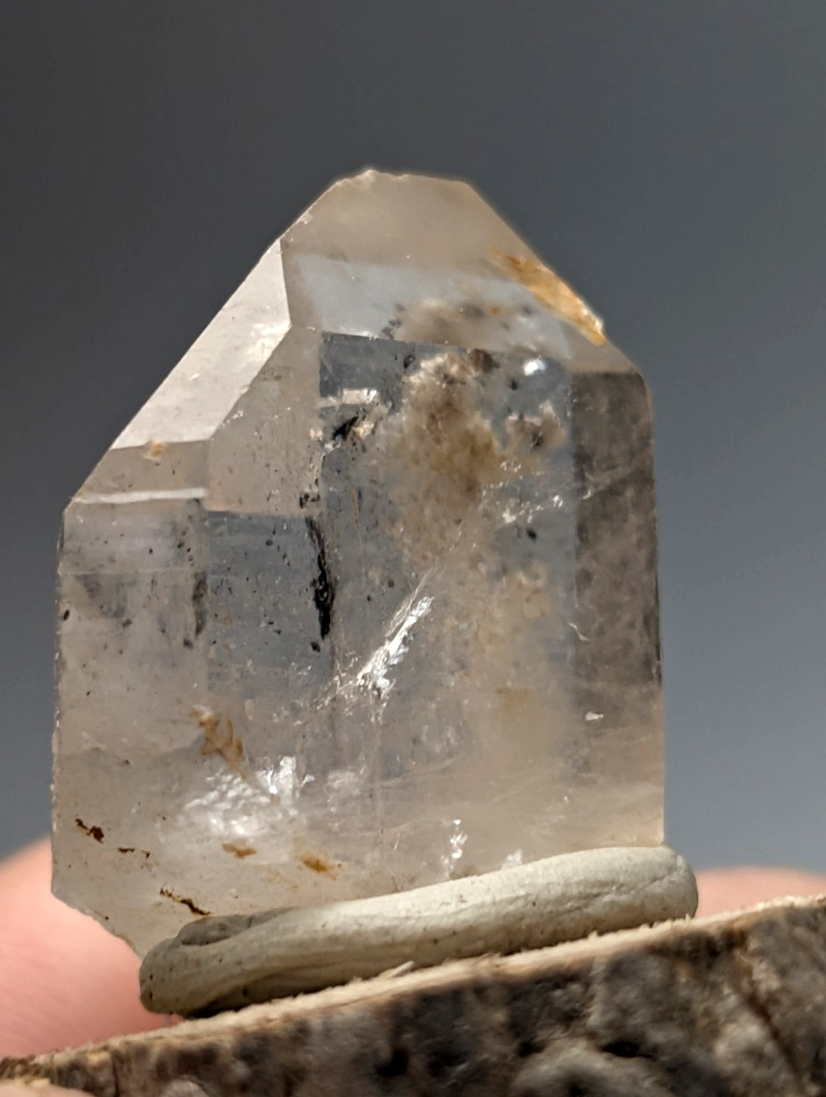 Translucent clear quartz crystal point with nacrite and manganese inclusions on wood base from arkansas