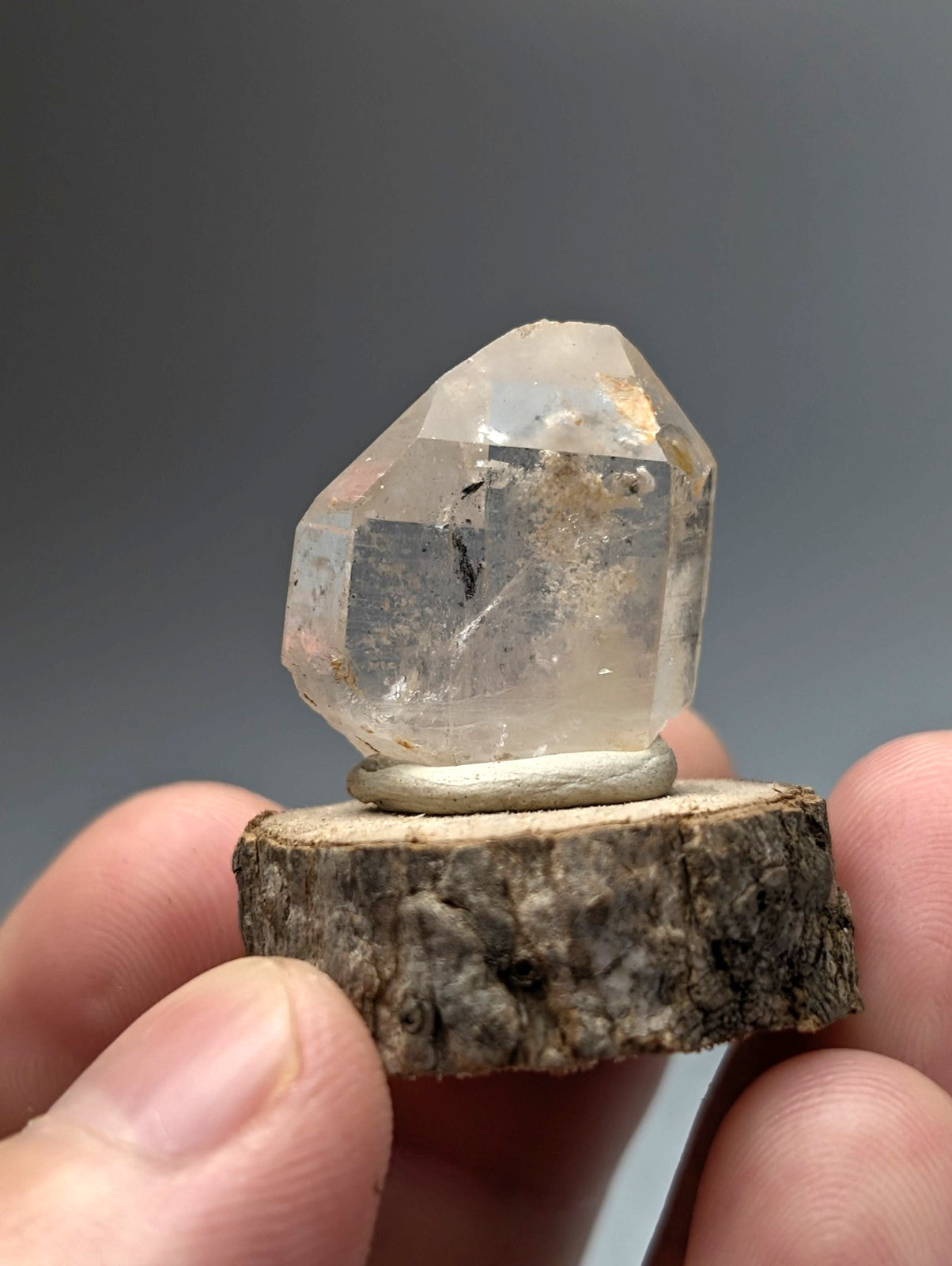 A clear nacrite and manganese included quartz crystal point with subtle inclusions on a rustic wooden base from arkansas