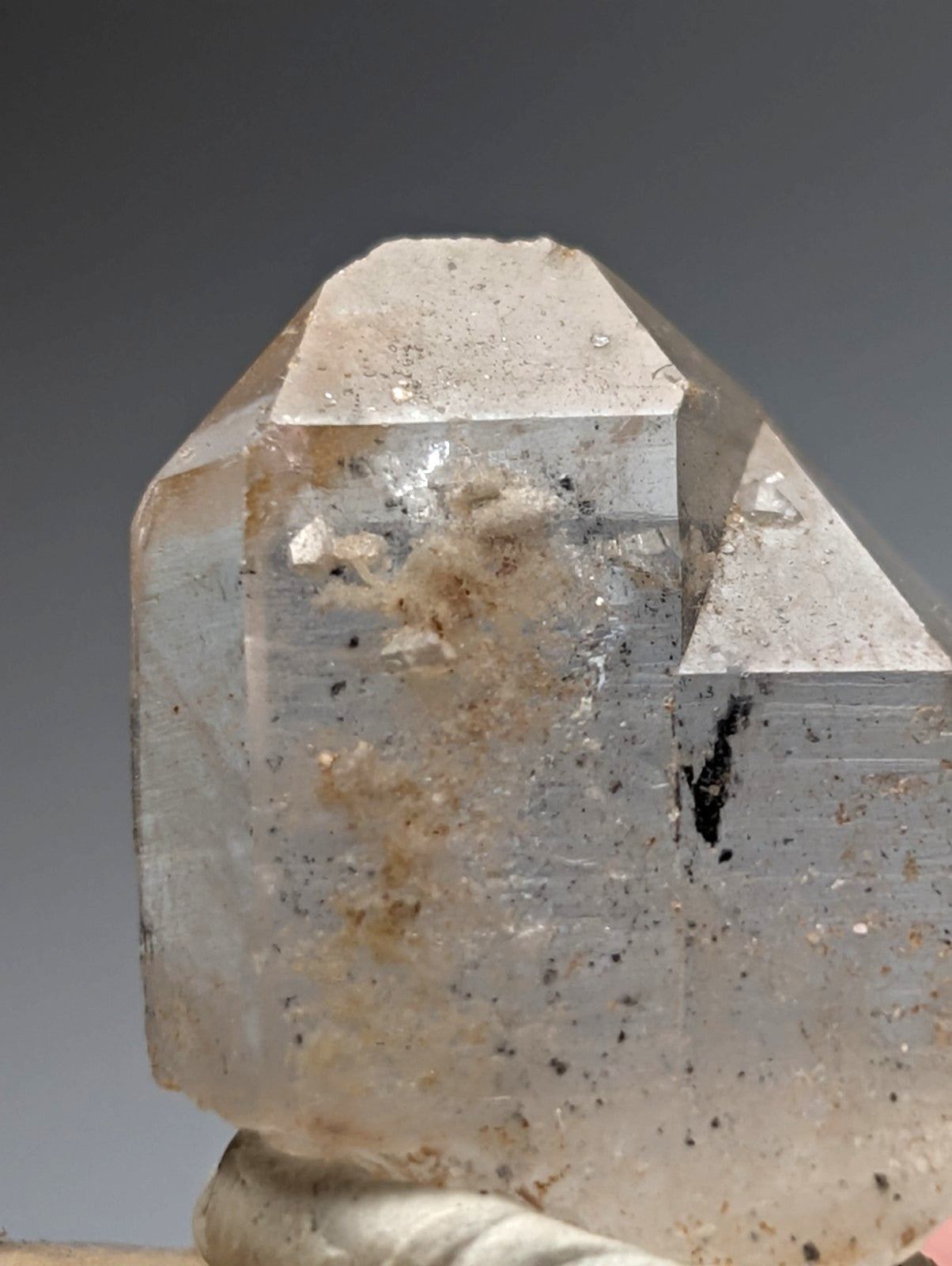 A translucent faceted quartz crystal point with nacrite and manganese inclusions on a wood base from arkansas