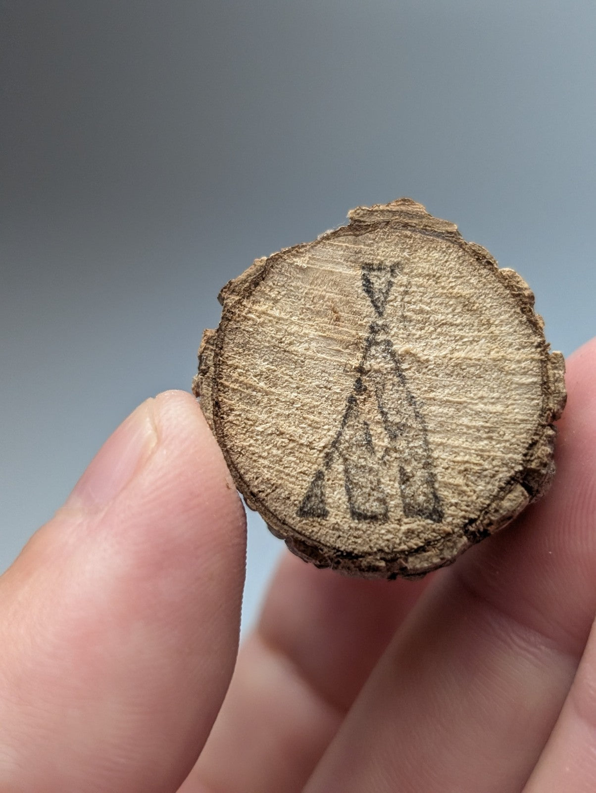 A rustic circular wood slice with light brown finish and engraved teepee design as a base for nacrite manganese quartz crystal point