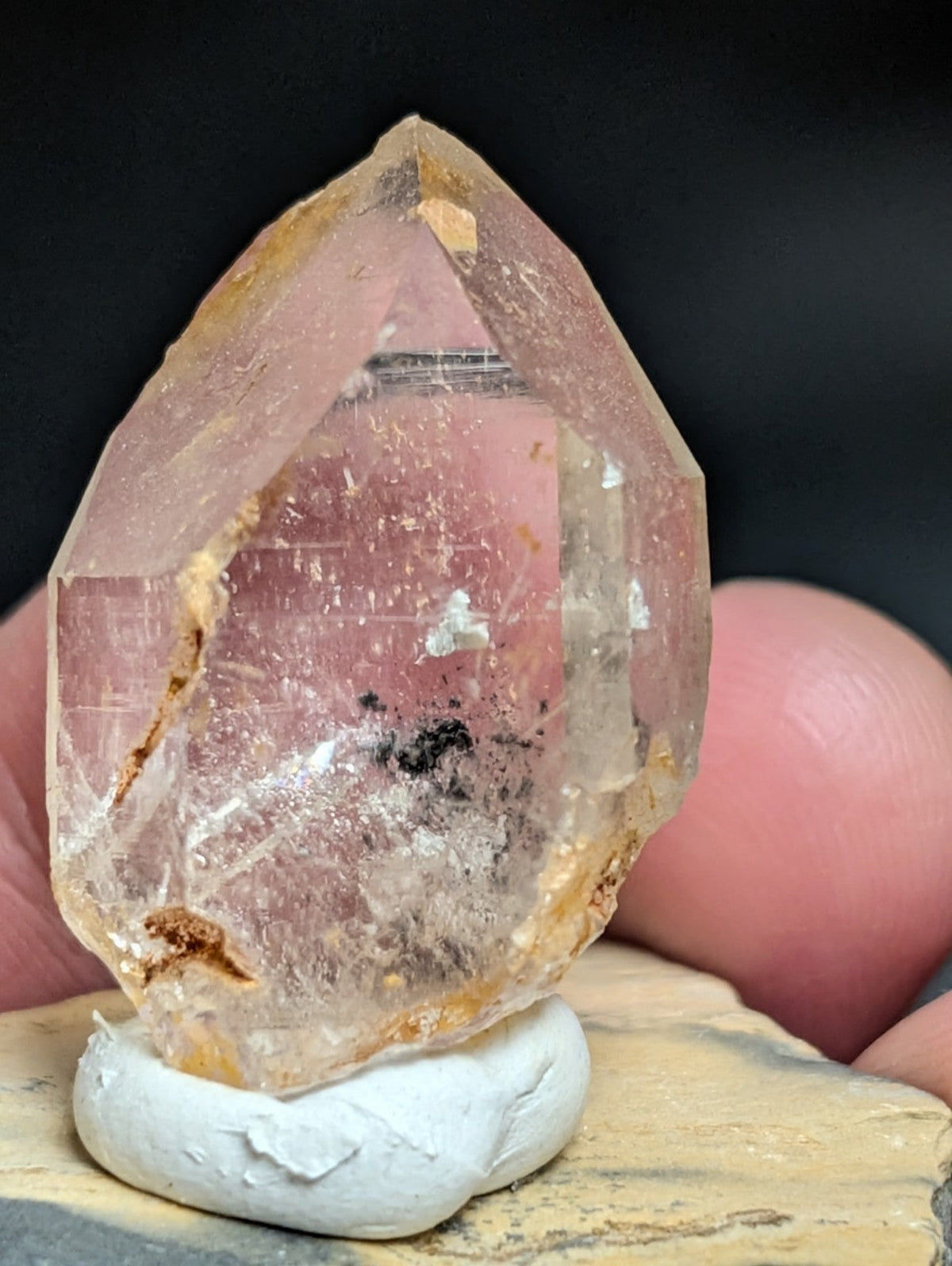 A translucent, pale pink quartz crystal with natural inclusions and golden-brown mineral veins.
